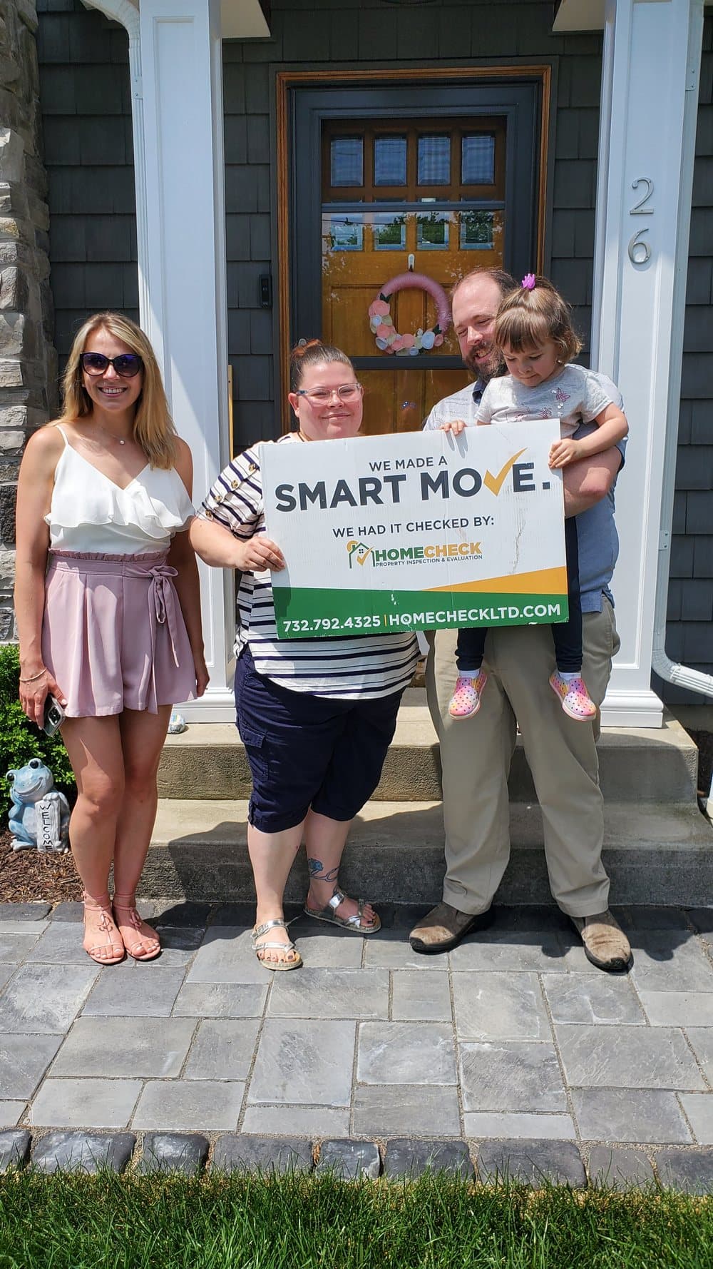 A family outside their newly inspected New Jersey home, holding a HomeCheck Smart Move sign